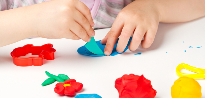 Child playing with colourful playdough on a table.