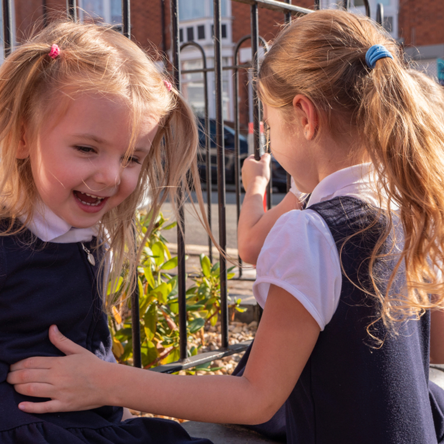 Two young primary school girls laughing together in the playground.