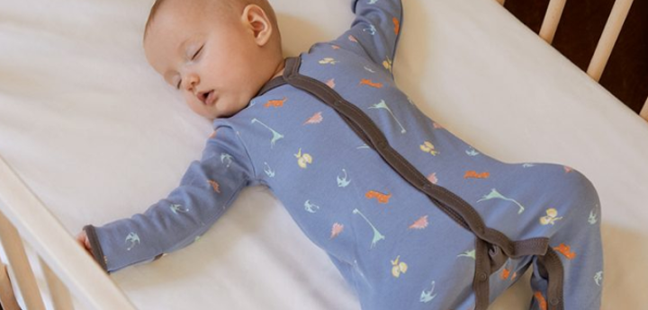 Baby lying in a cot with their arms stretched out