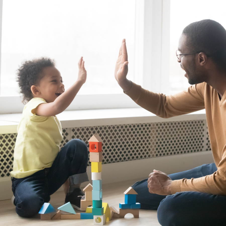 Young child and adult high-fiving whilst sitting on the floor.