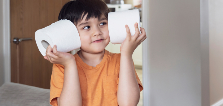 Young boy smiling holding two toilet rolls up to his face.