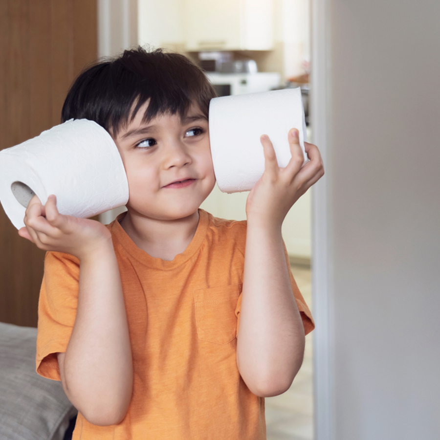 Young boy smiling holding two toilet rolls up to his face.