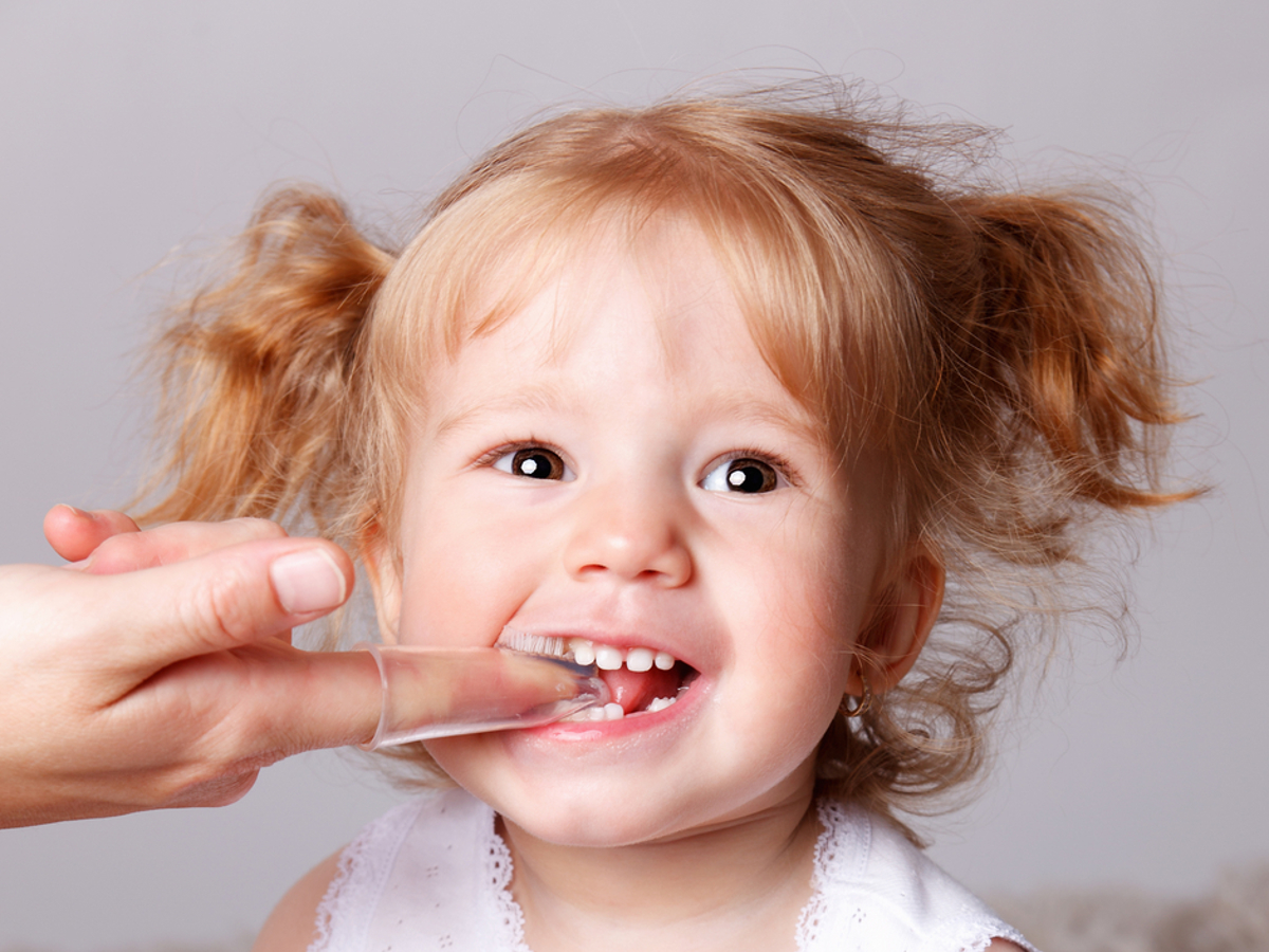 adult hand using a finger toothbrush on a young girl