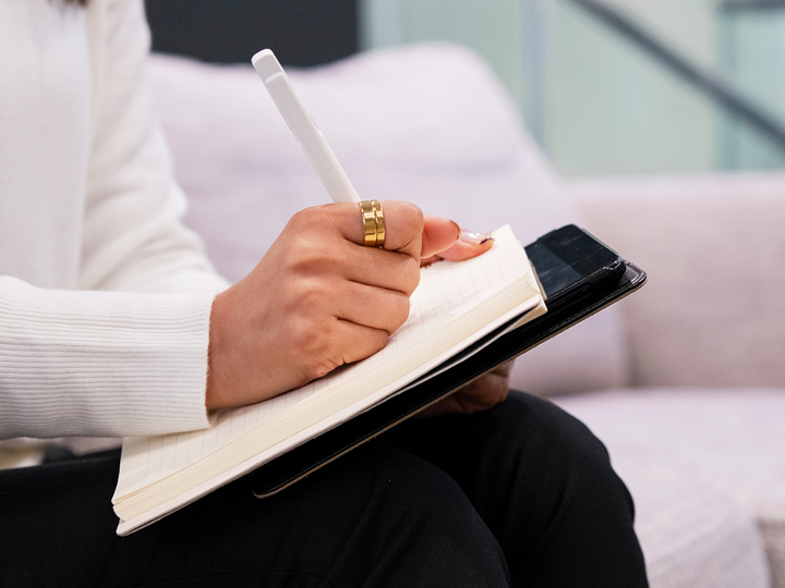 woman writing on a notepad on top of a tablet