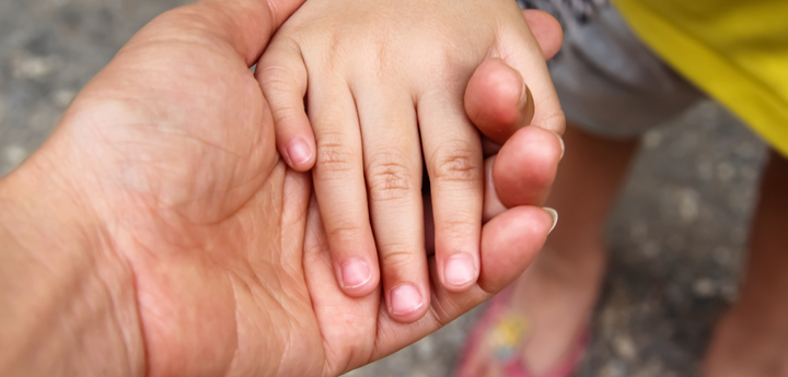 An adults hand is outstretched and a small child has placed their hand in the adults