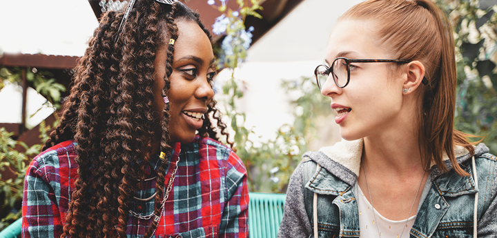 2 teenage girls talking. Girl on left is holding a phone