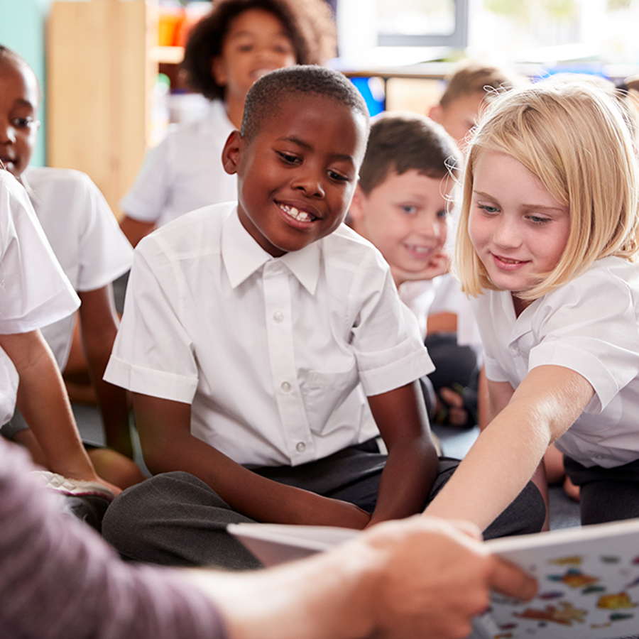 Children in a class looking at a book held by a teacher.