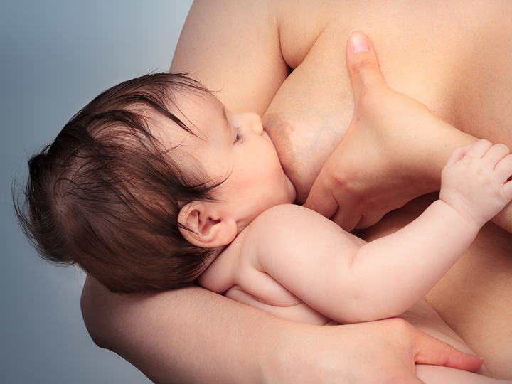 Adult holding their breast whilst breastfeeding their baby.