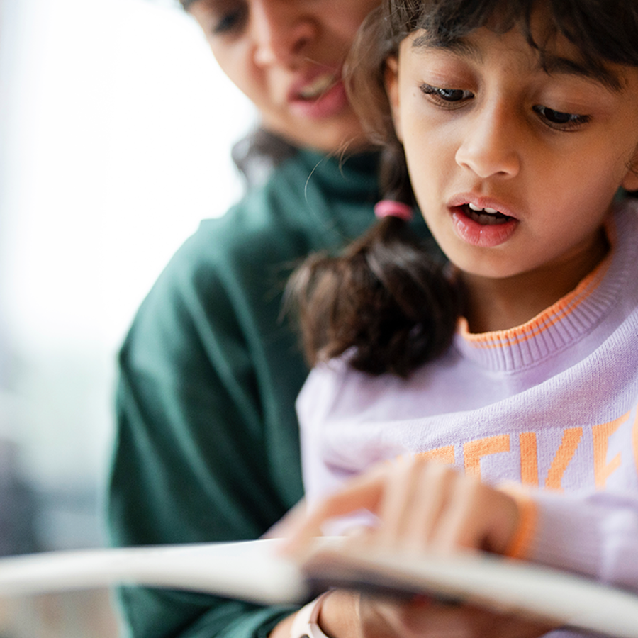 Child sitting on the lap of an adult reading out loud.