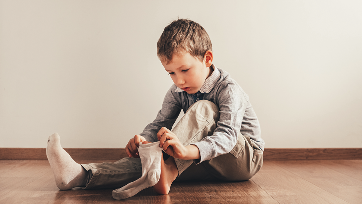 Boy sitting on the floor putting on a sock.