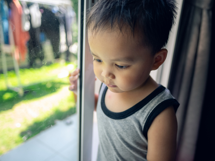 Young child standing and holding sliding glass door and looking down to the ground with garden in background