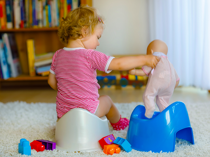 Child sitting on a potty playing with a doll on another potty.