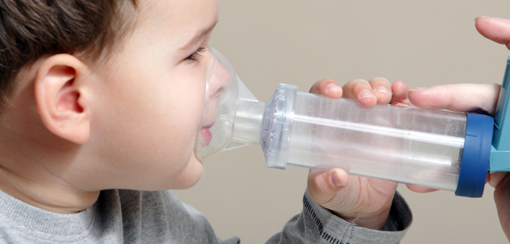 Young boy holding a spacer with an inhaler attached to his face