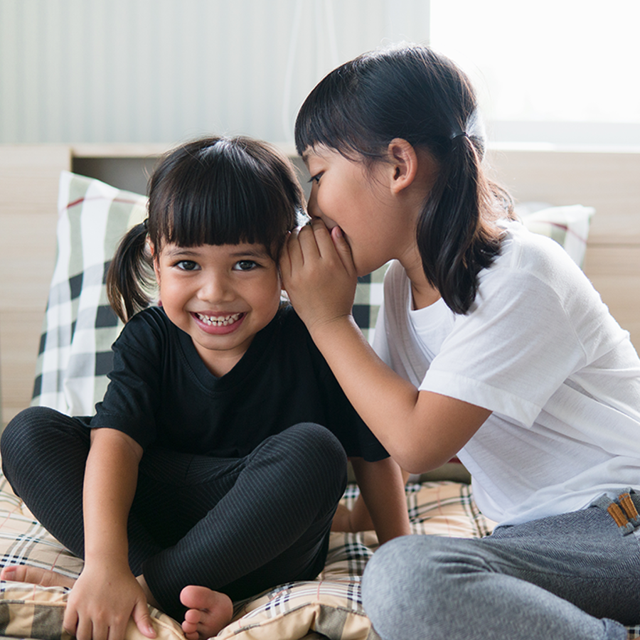 girl whispering into ear of laughing friend