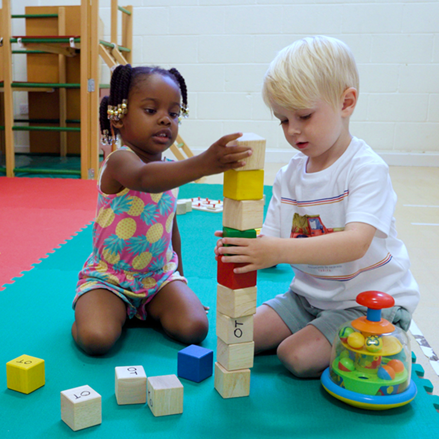 2 children playing with blocks on a foam floor in an occupational therapy room.