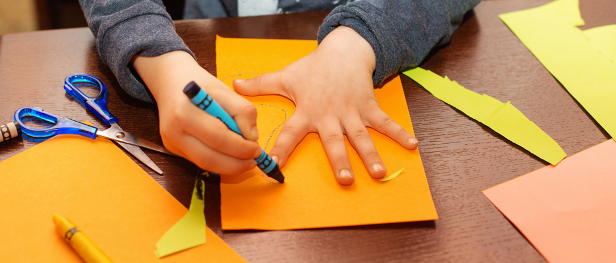 Child tracing hand with blue crayon on orange paper.