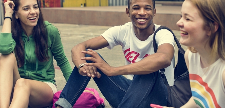 Three teenagers sitting on the ground laughing with each other