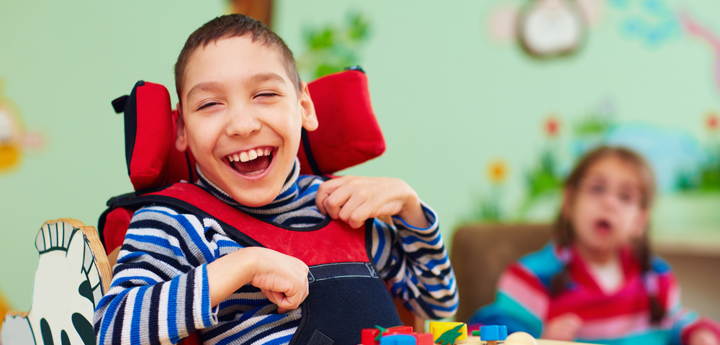 Young boy with cerebral palsy laughing whilst sitting in a chair with a toy in front of him