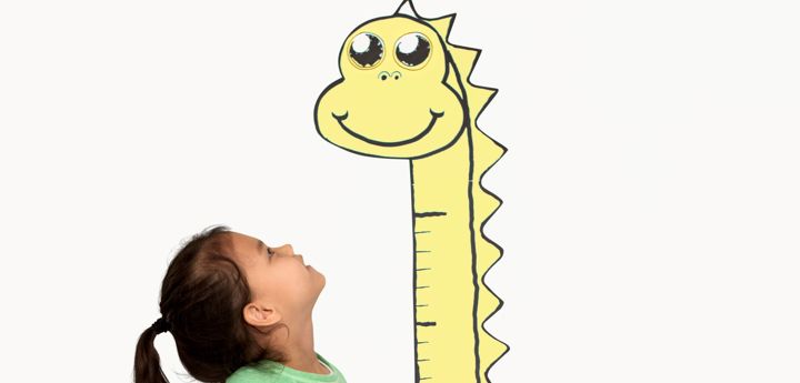 A girl standing next to a cartoon giraffe, looking up at its long neck and head.