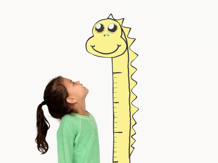 A girl standing next to a cartoon giraffe, looking up at its long neck and head.