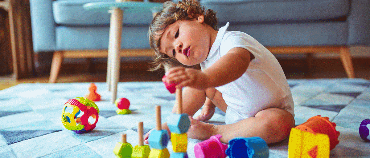 Toddler sitting on the floor in a sitting room, playing with toys on the carpet.