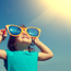 Young girl smiling whilst wearing oversized yellow sunglasses looking up at the sky.