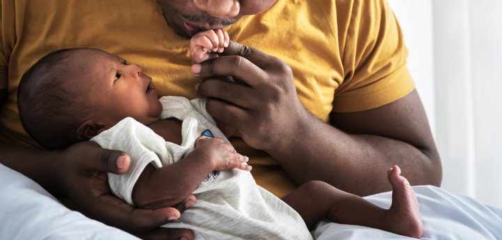 A dad holding a newborn baby in his arms and kissing their hand