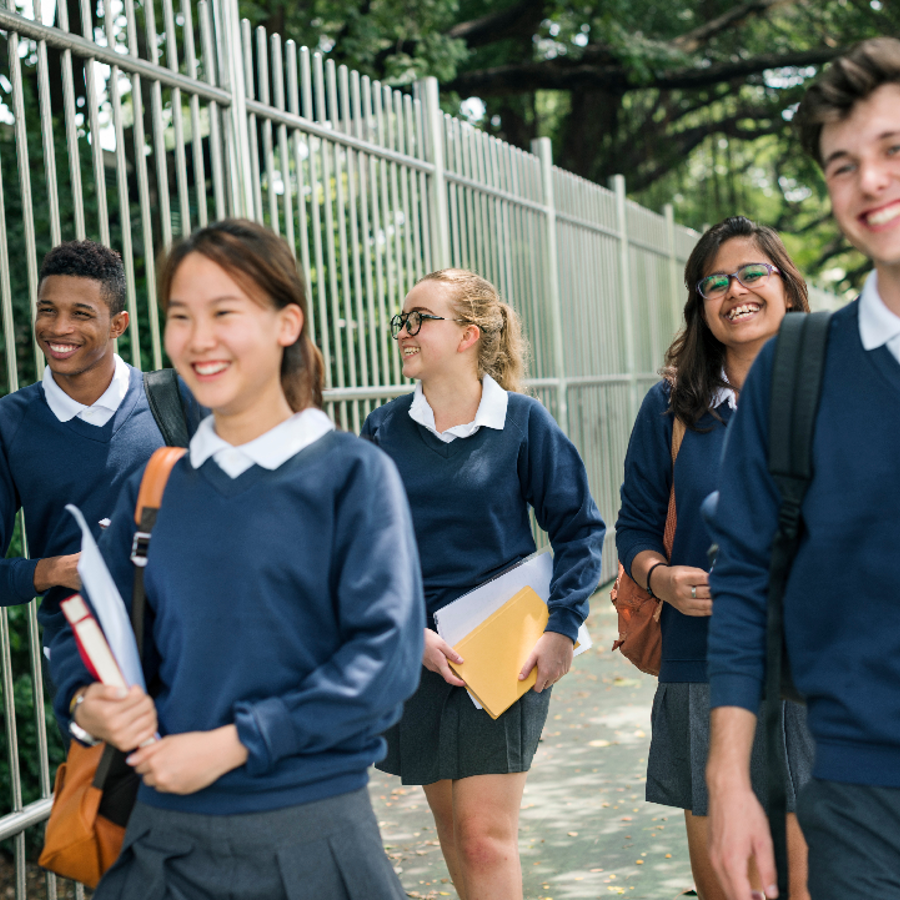 Five teenagers in school uniform smiling and laughing whilst walking down the road.