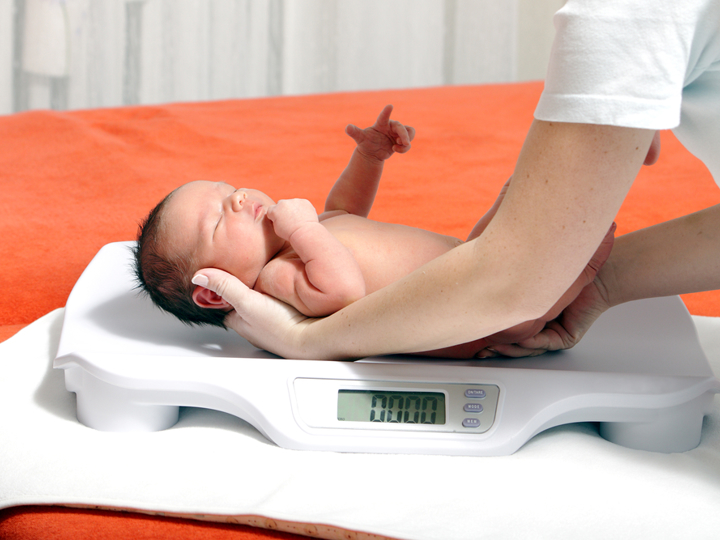 Naked new-born baby being laid on scales by an adult.