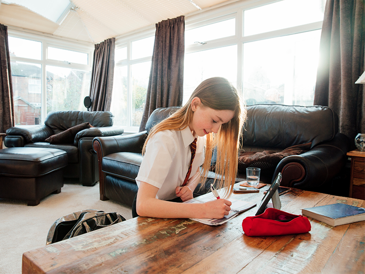 Girl sitting on the floor in a living room, doing homework on the coffee table.