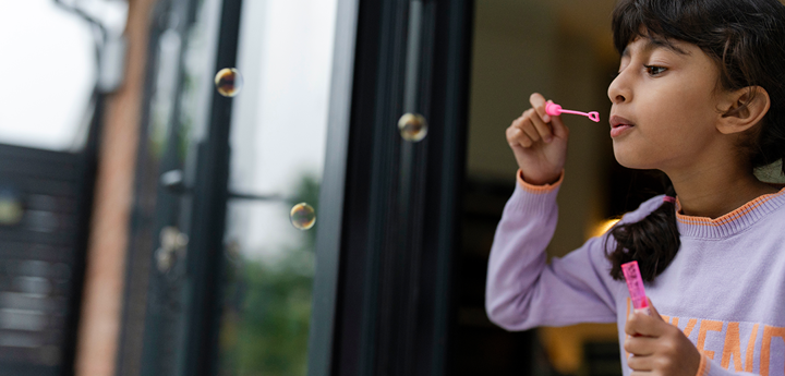 Girl blowing bubbles into a garden.