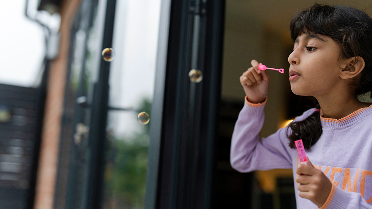 Girl blowing bubbles into a garden.