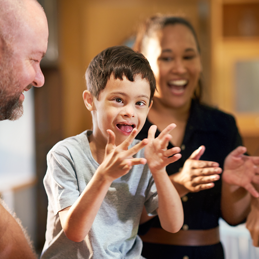 Boy with cerebral palsy with their family. The boy and family are smiling and clapping 