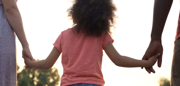 Young girl walking holding hands with two adults either side.