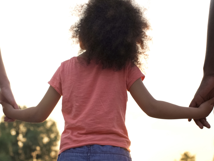 Young girl walking holding hands with two adults either side.