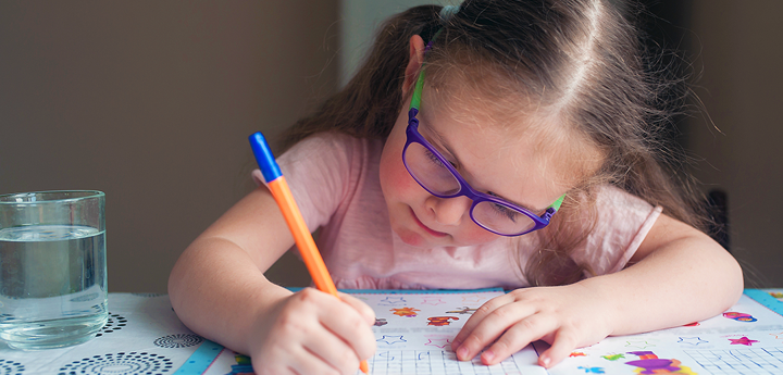 Girl Writing In Activity Book Wearing Glasses