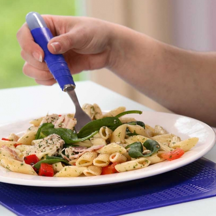 Person using ergonomic cutlery on a plate full of pasta. The plate is on a non-slip mat.