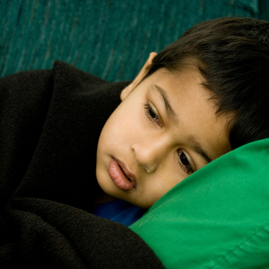 Young boy looking unwell lying on sofa under a blanket