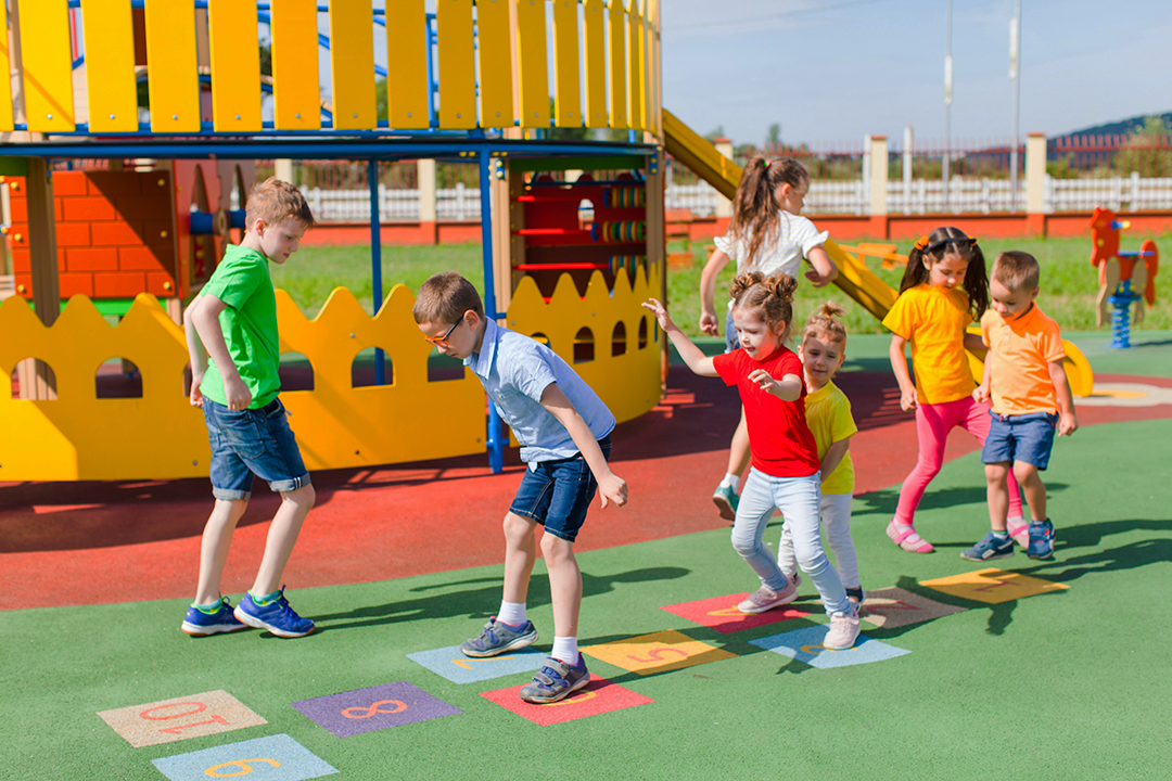 7 children in playground playing hopscotch