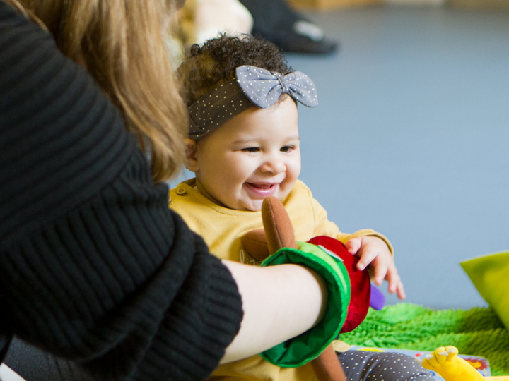 A child giggling with a lady sitting in front of the child with a hand puppet on.