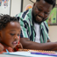 Young child and adult sitting down looking at a notebook