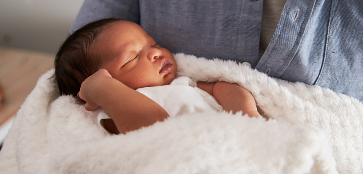 Young baby being held by a woman as they sleep wrapped up in a white fluffy blanket.