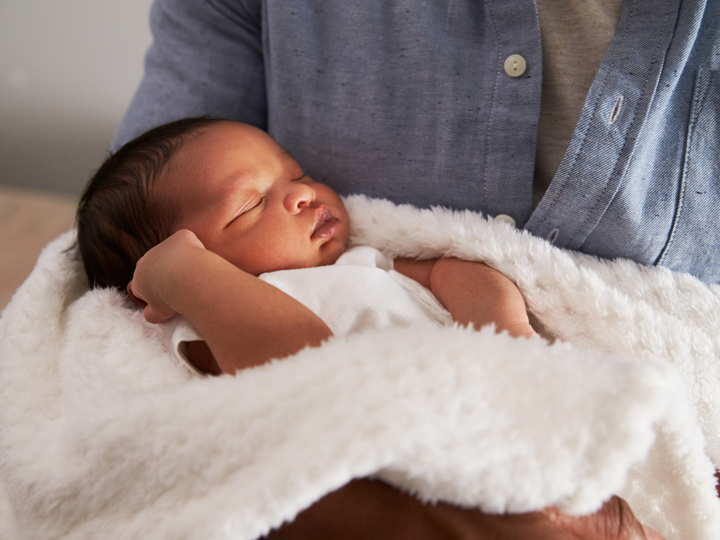 Young baby being held by a woman as they sleep wrapped up in a white fluffy blanket.